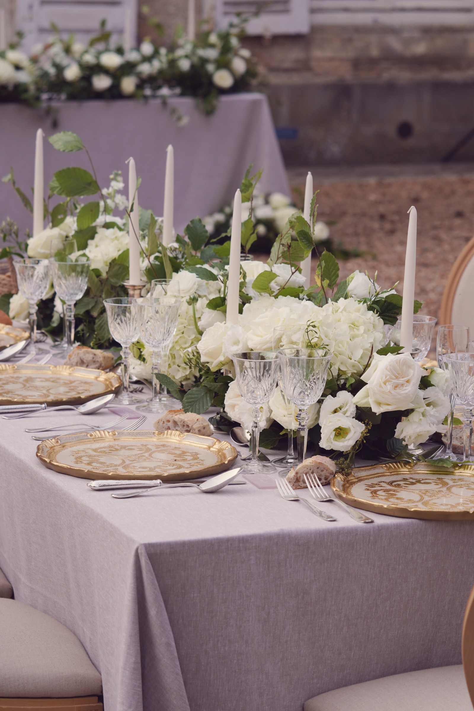 Reception tablescape with white florals, taper candles, gold chargers and grey linen at Château de Bouthonvilliers