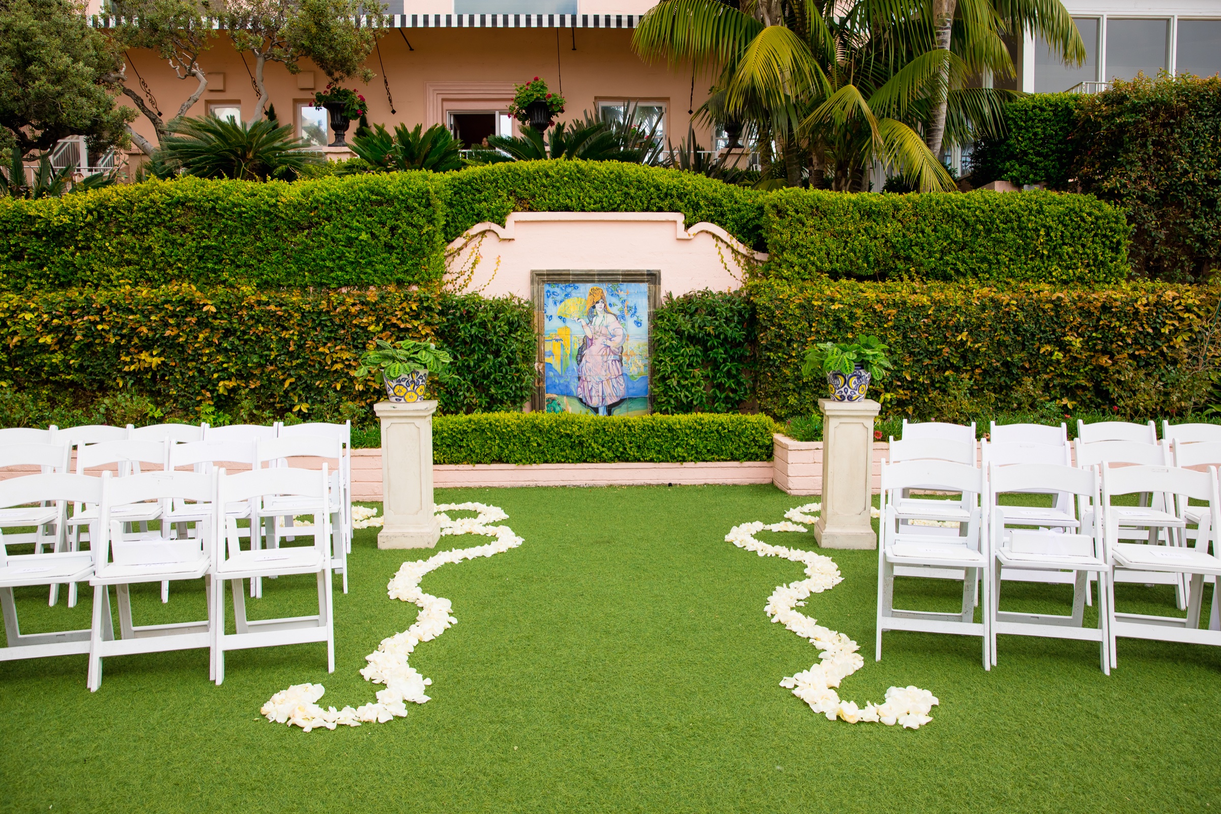 El Jardín ceremony at La Valencia Hotel with a tile mural altar, stone pedestals, and a cream petal aisle