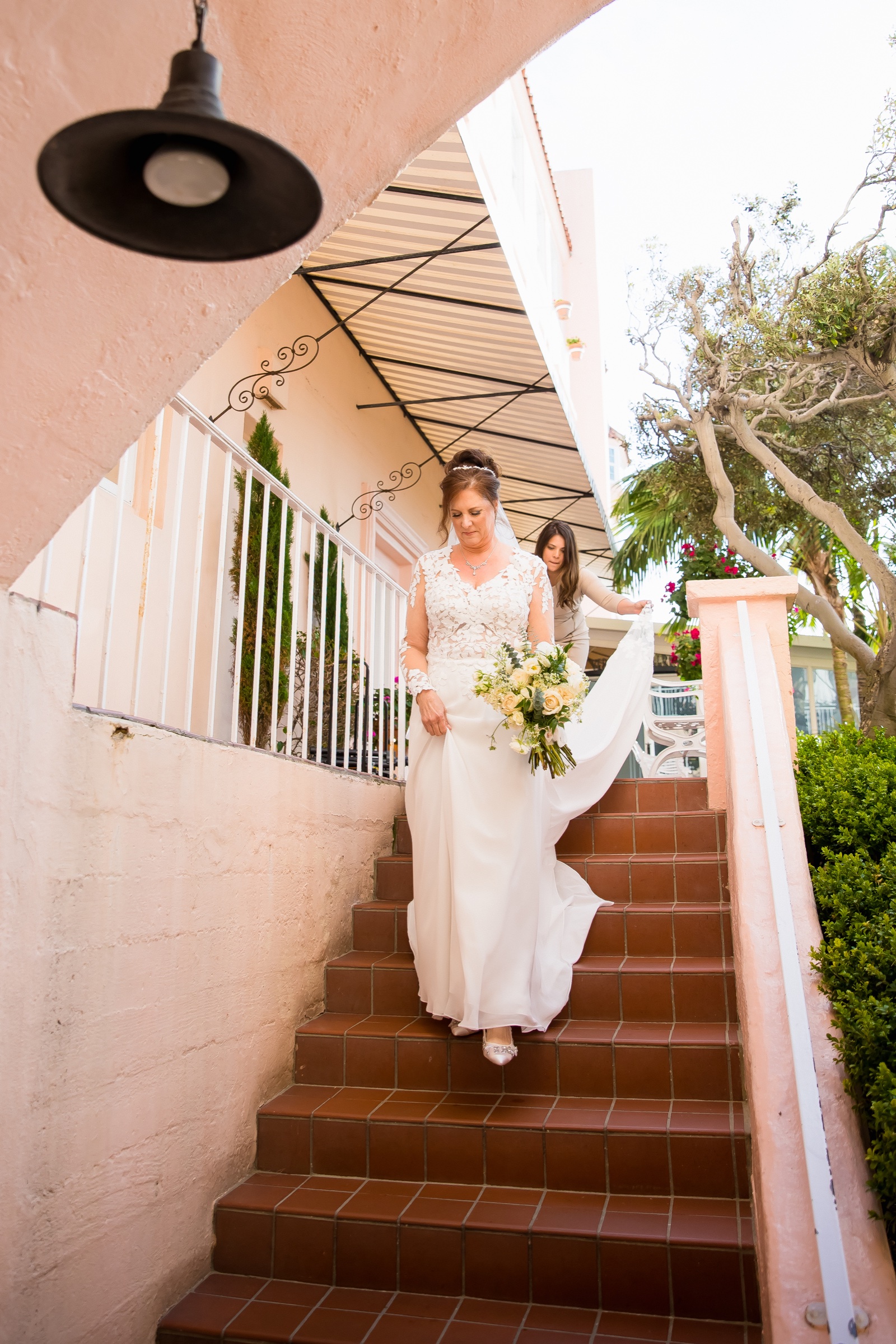 Bride descending the terracotta stairs at La Valencia Hotel with a cream rose and eucalyptus bouquet