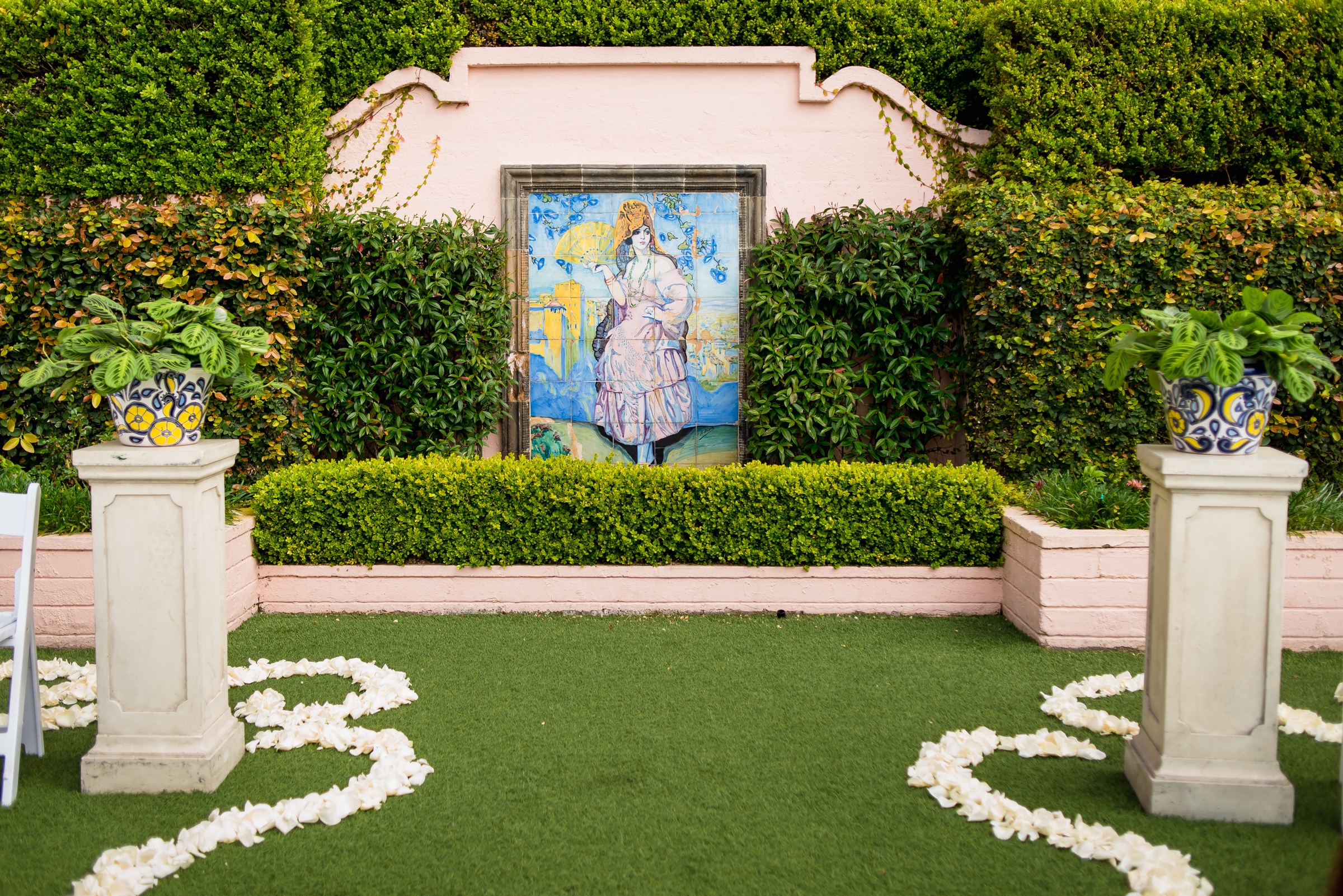 Hand-painted tile mural altar with Spanish ceramic pots on stone pedestals at El Jardín