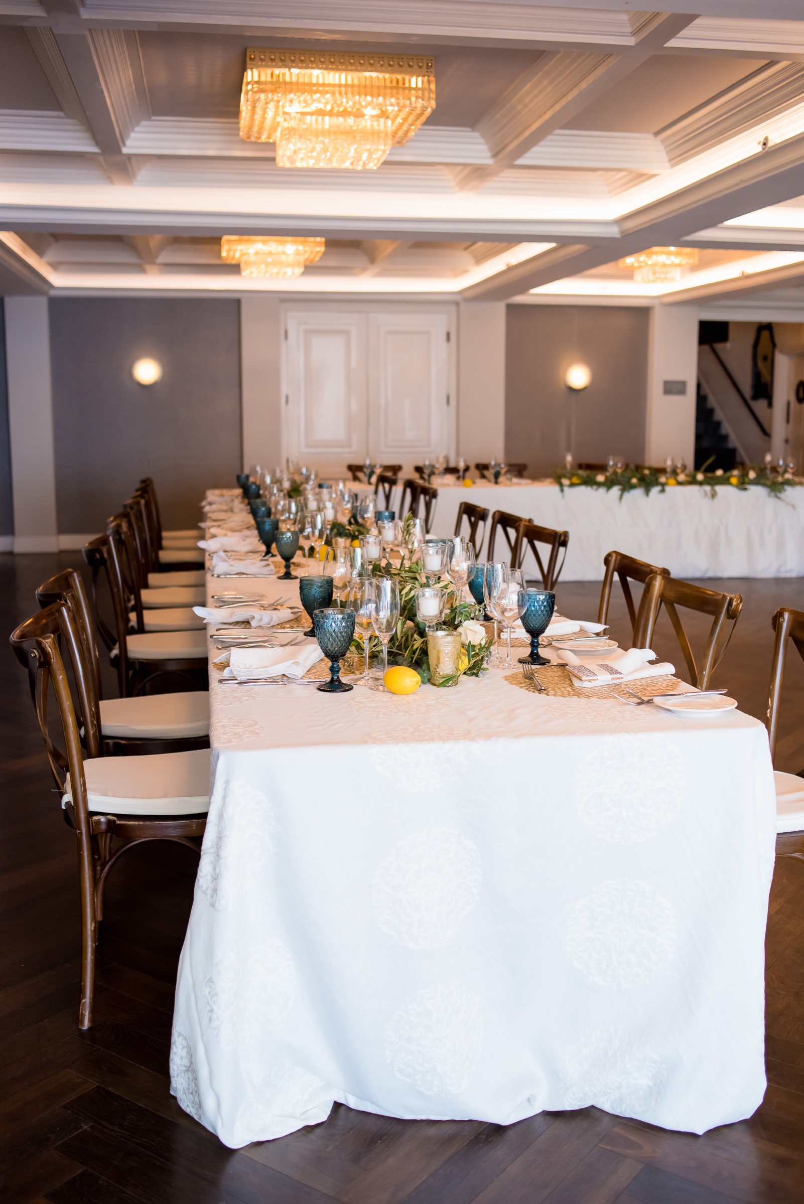 Long dinner table in the Salon at La Valencia Hotel with crossback chairs, blue hobnail goblets, and a lemon garland