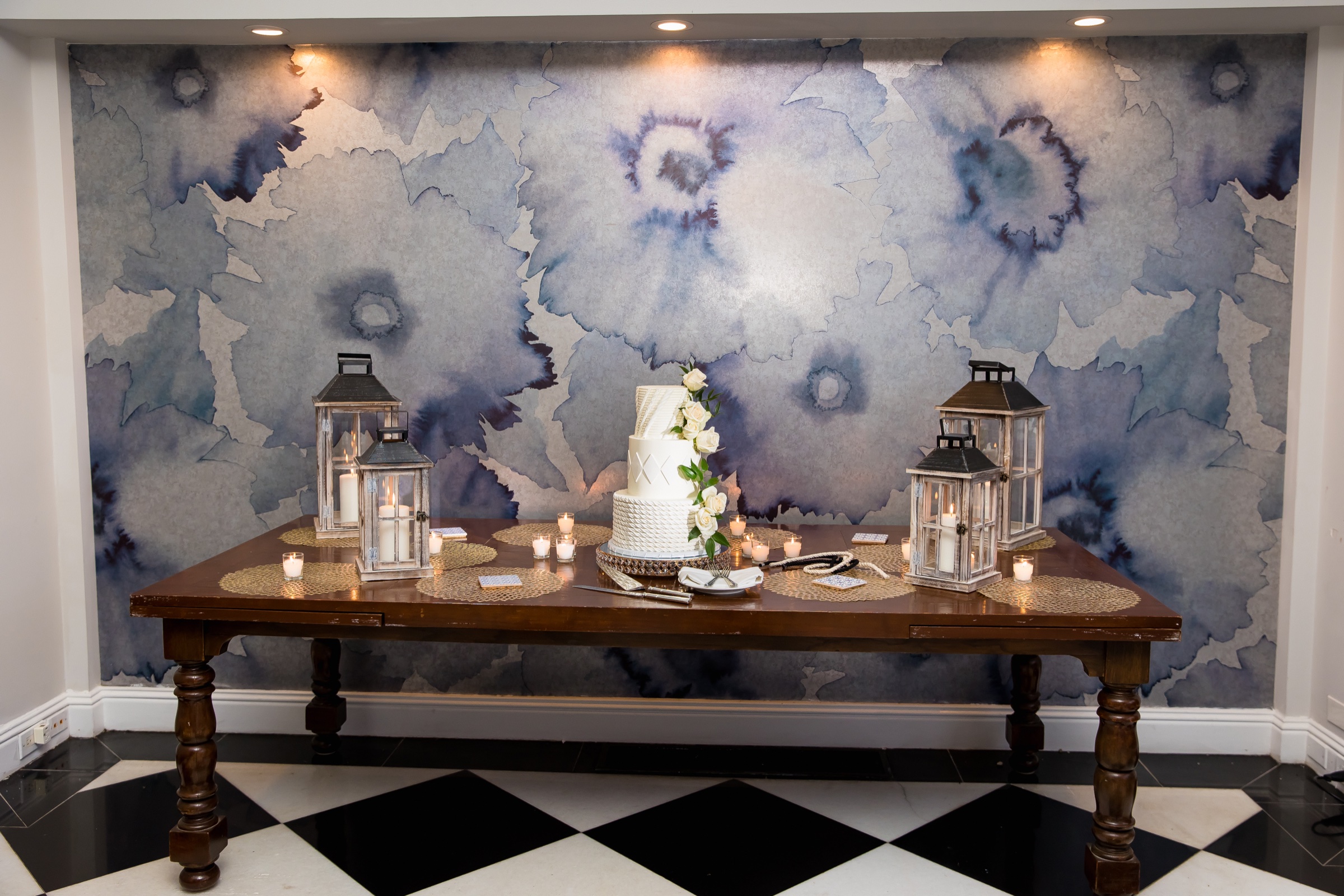 Cake table with white lanterns against the blue floral wall in the Veranda Ballroom