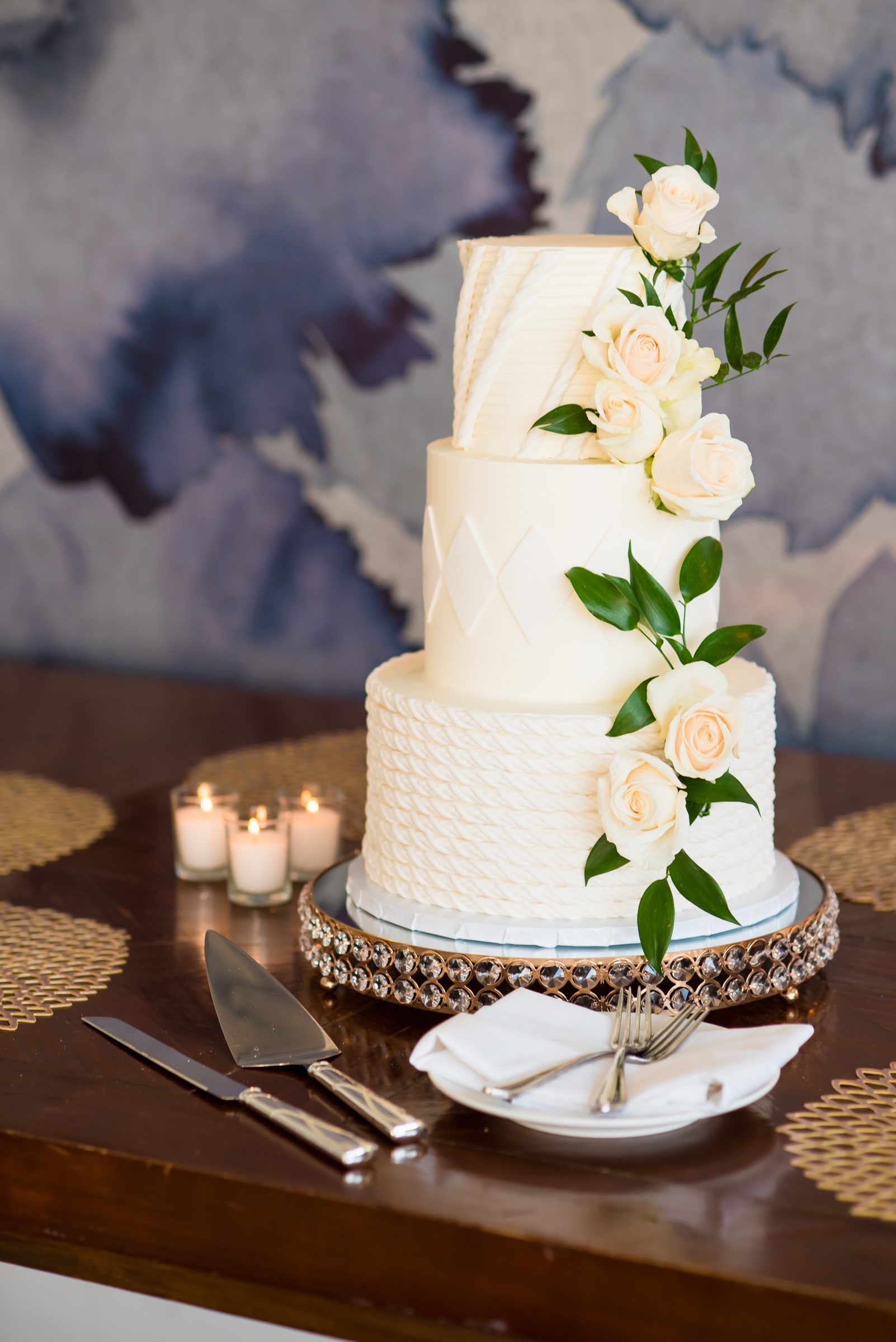 Three-tier cream wedding cake with rope and quilt texture and cream roses by The Fabulous Cake Girls