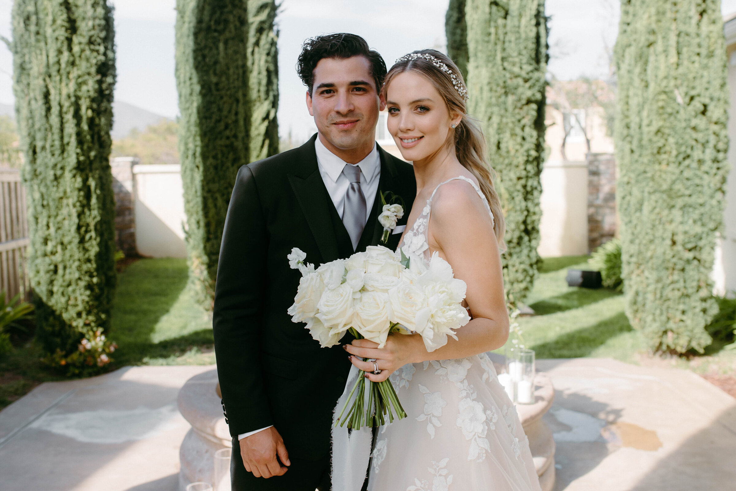Erika and Julio with a white rose bouquet between cypress trees at their private estate wedding in San Diego