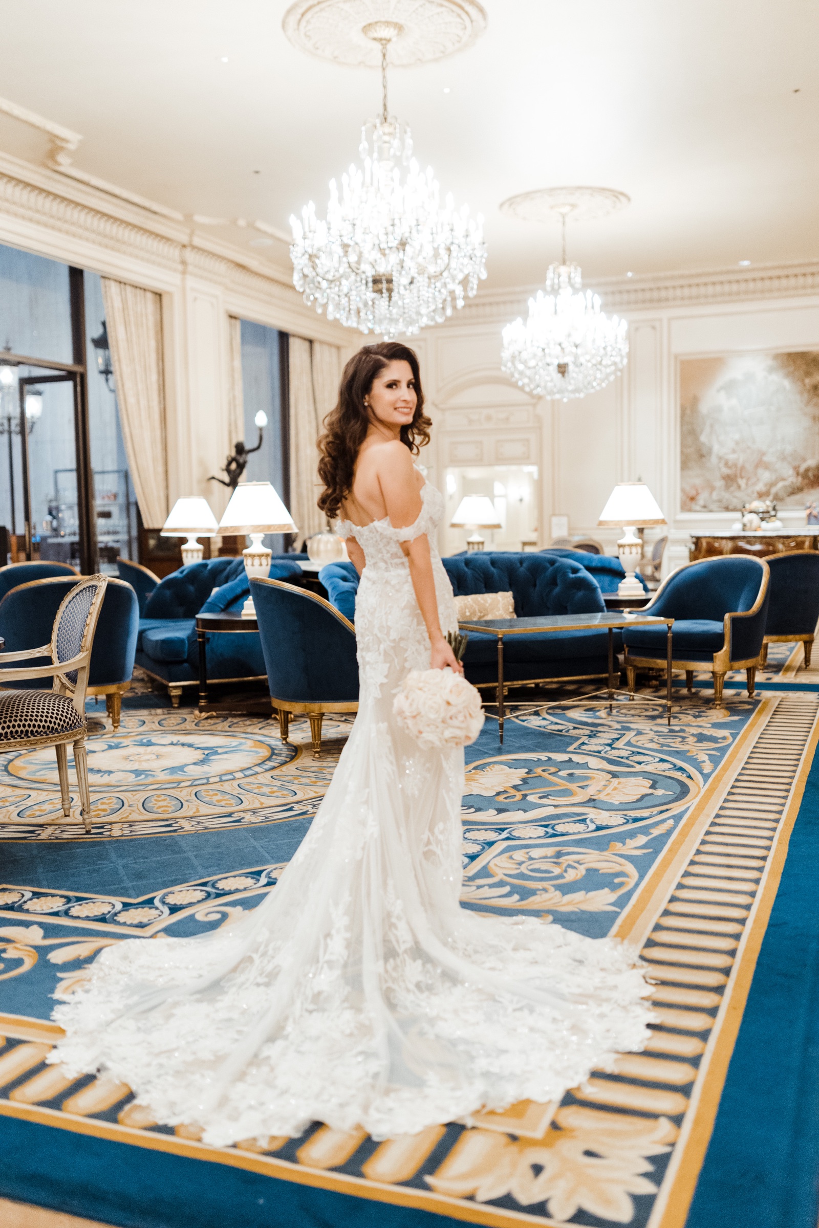 Bride in a lace gown with a cream bouquet on the blue carpet of The Westgate Hotel lobby