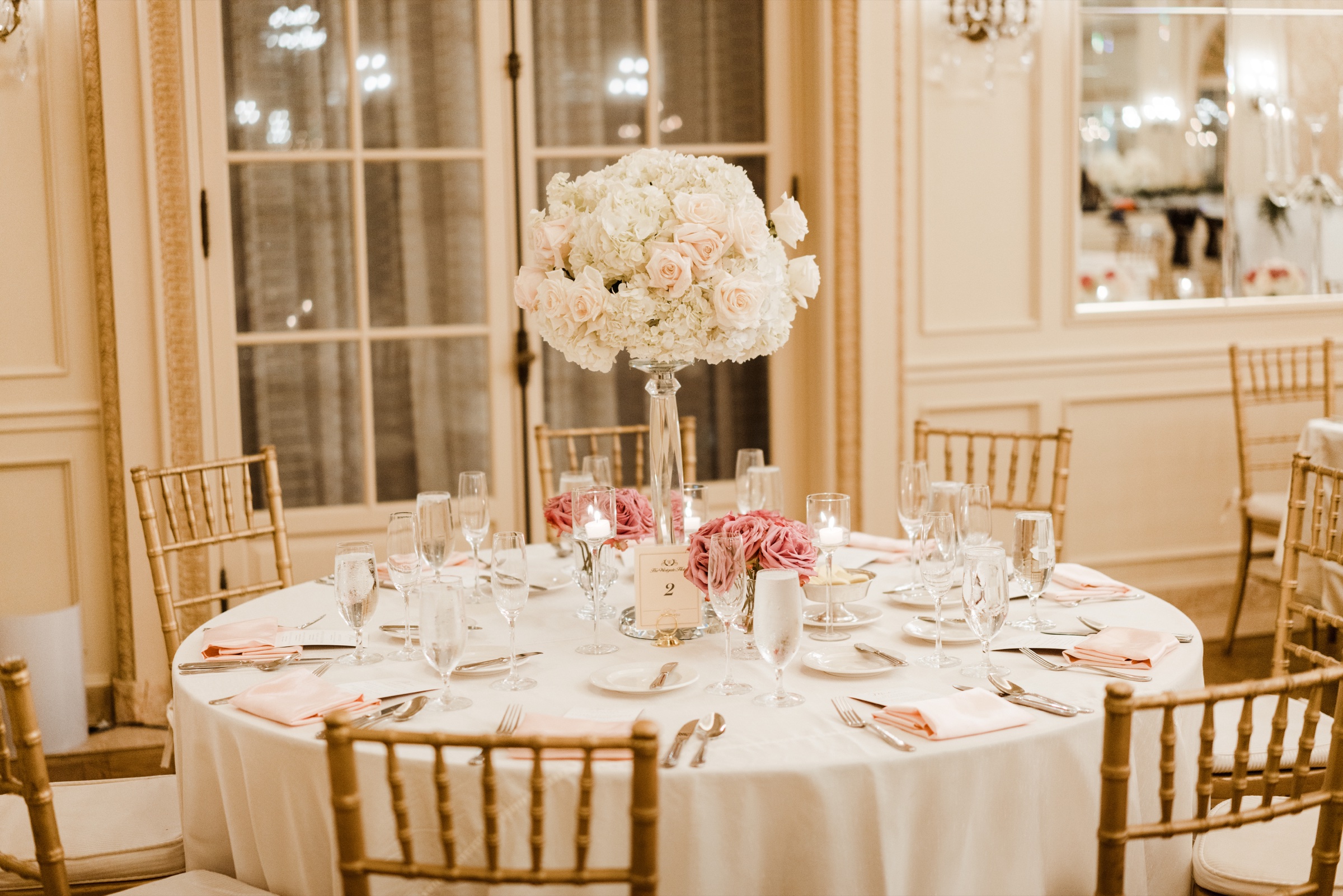 Reception table centerpiece of white roses with a gold candelabra and crystal glassware